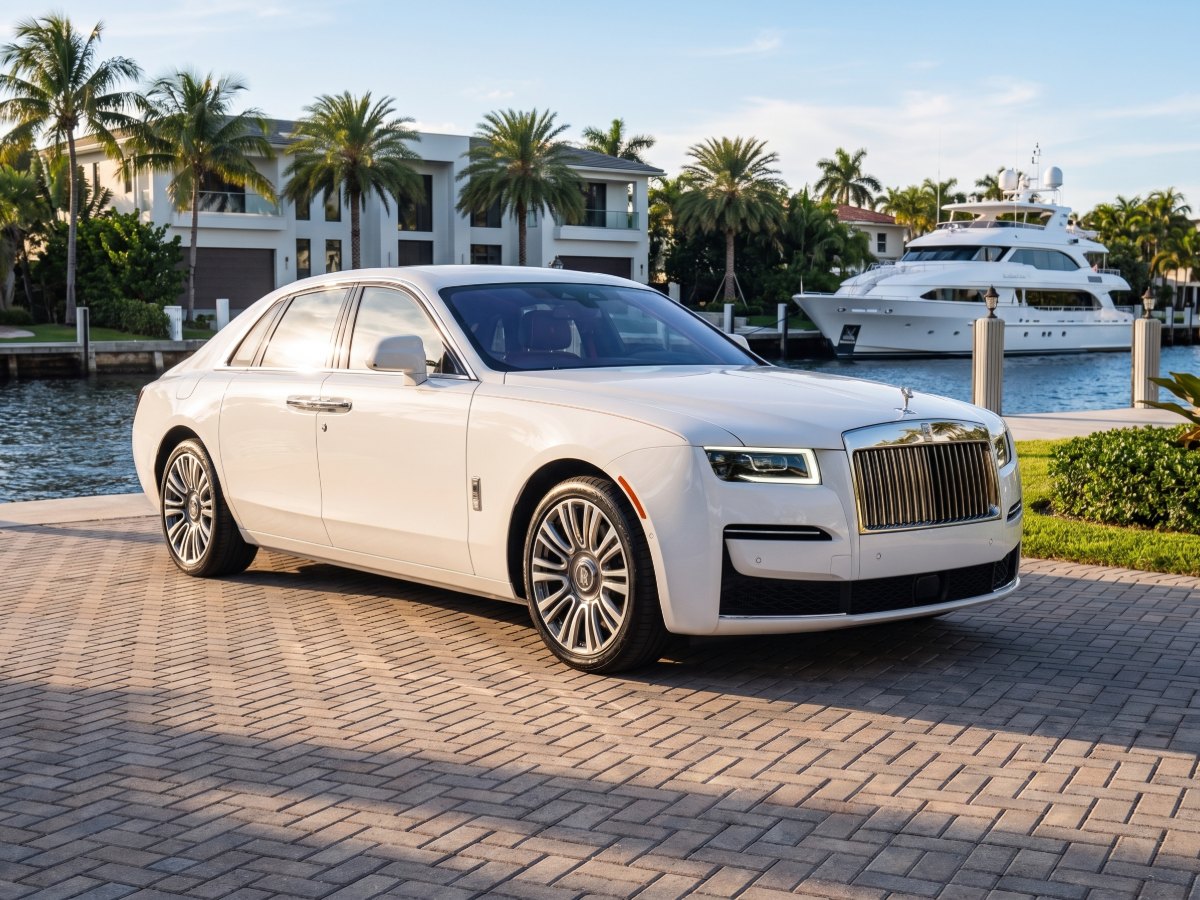 White Rolls-Royce Ghost at a waterfront home with a yacht behind it